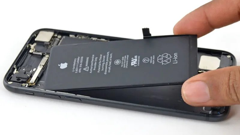 Tay cầm pin iPhone được tháo từ bên trong vỏ máy, hiển thị mặt sau pin có in logo Apple và thông số kỹ…