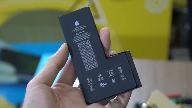 Hình ảnh pin iPhone đen được cầm trên tay, hiển thị logo Apple và các biểu tượng cảnh báo an…